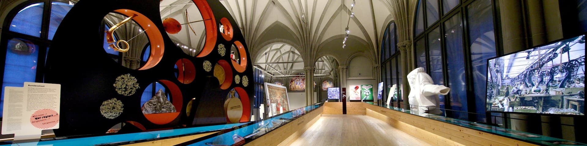 A museum interior with a large circular sculpture, wooden floors, and arched ceilings.