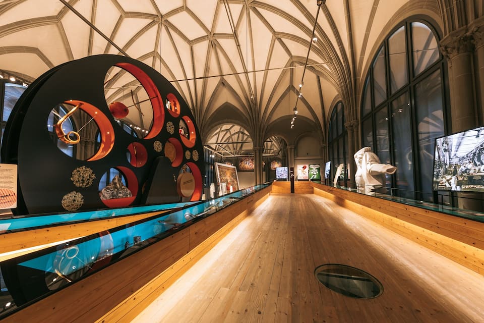 A museum interior with a wooden floor, large circular art installations, and a display of historical artifacts.