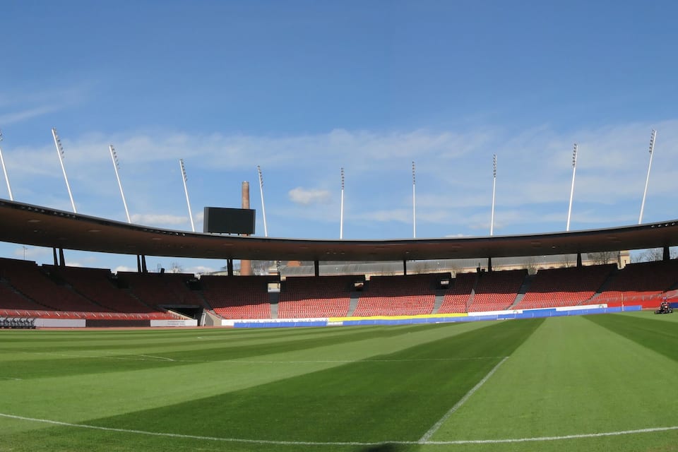 A large, empty stadium with a green field and red seating.