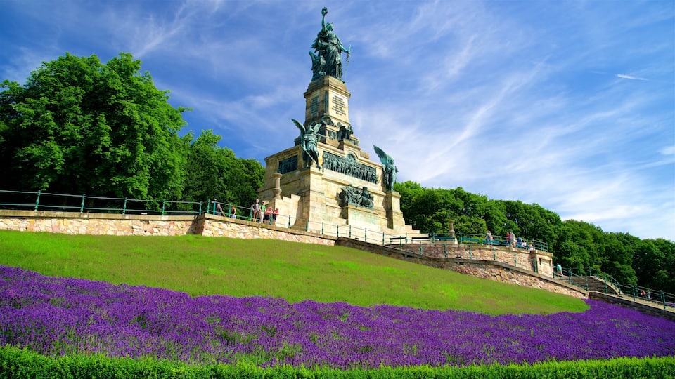 A monument with a statue on top, surrounded by a grassy area with purple flowers.