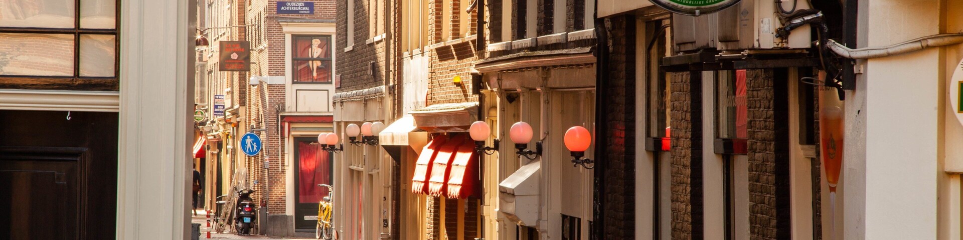 Una calle estrecha con arquitectura tradicional europea, un letrero de Heineken y una bicicleta estacionada en la acera.