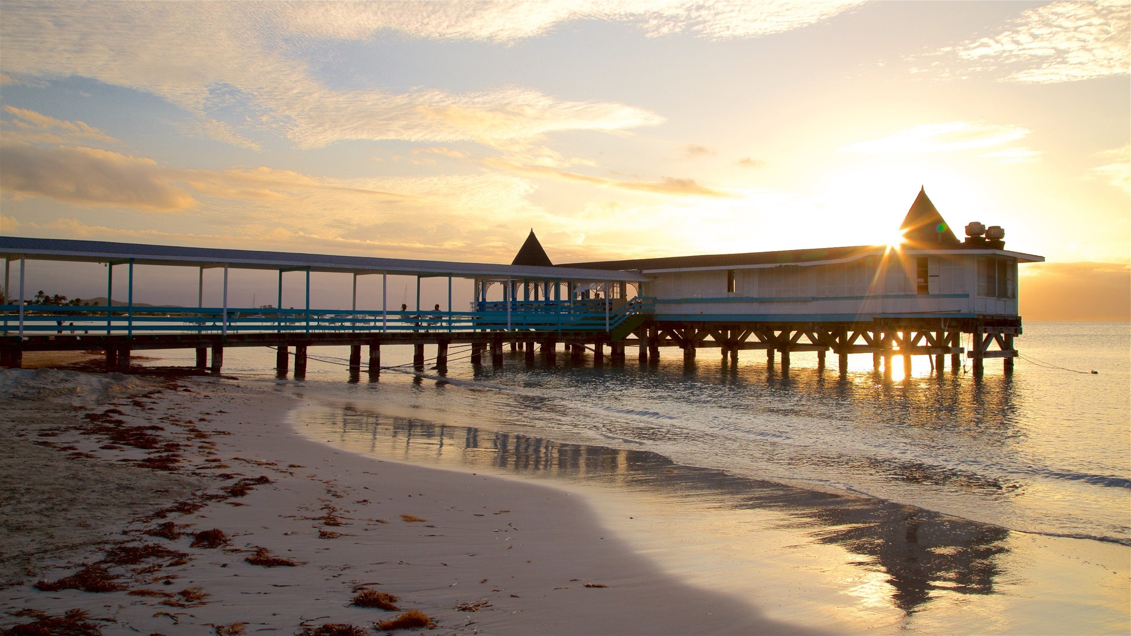 A pier extending into calm waters at sunset with a beach in the foreground.