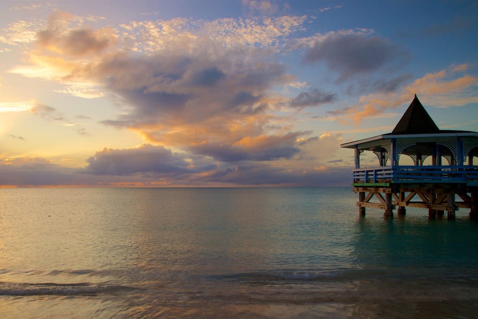 Un muelle se adentra en aguas tranquilas al atardecer, bajo un cielo despejado.