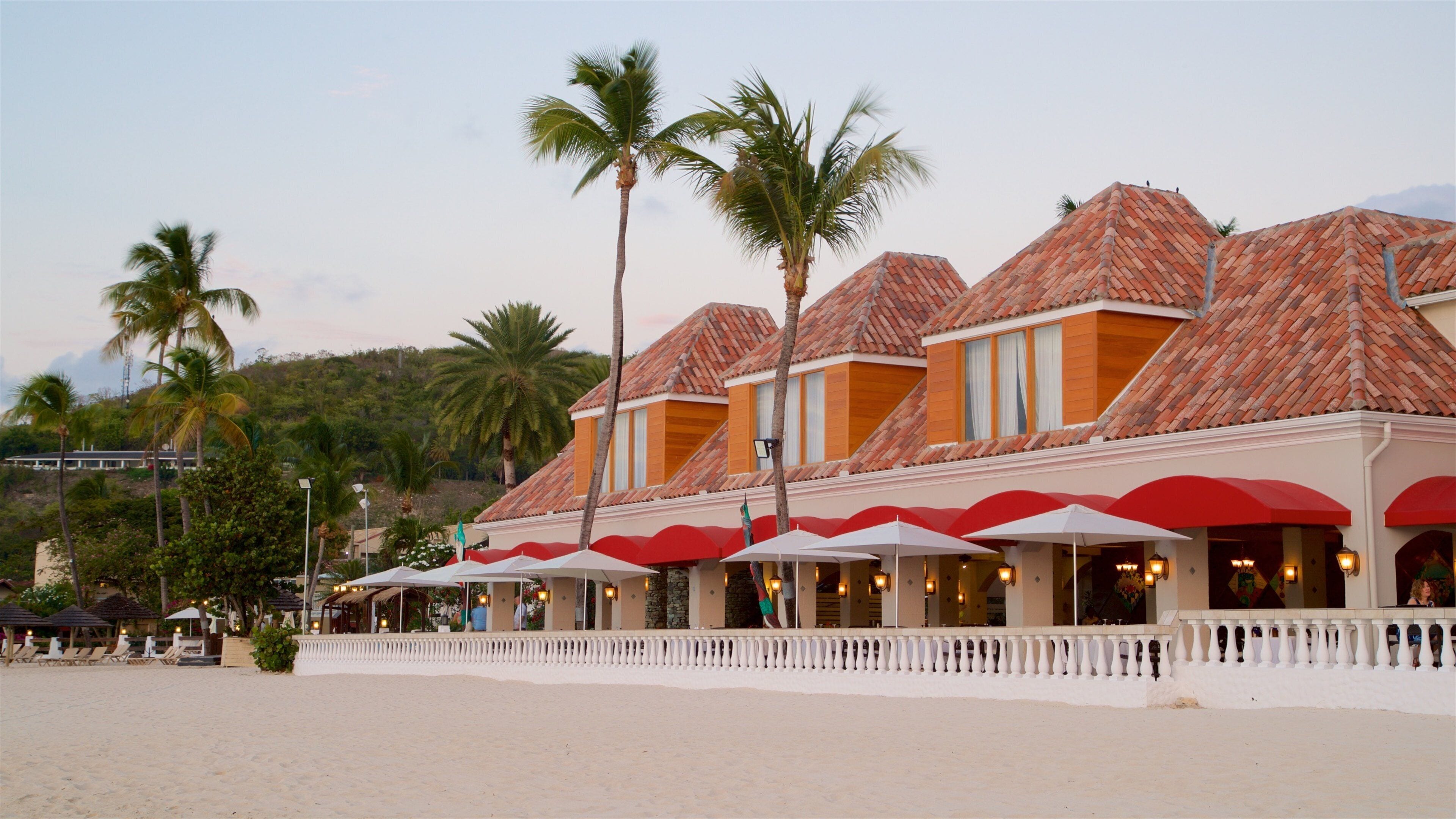 A beachfront resort with palm trees, red umbrellas, and a sandy beach.