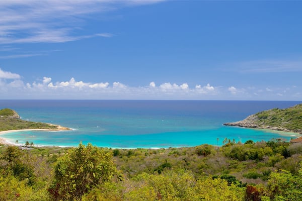 A coastal landscape with turquoise waters, a sandy beach, and lush greenery.