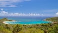 Een kustlandschap met turquoise water, een zandstrand en weelderige begroeiing.