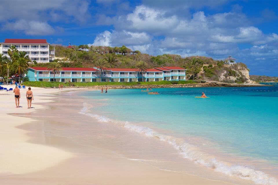 Een strand met helder turquoise water, een zandstrand en een resortgebouw met meerdere balkons.