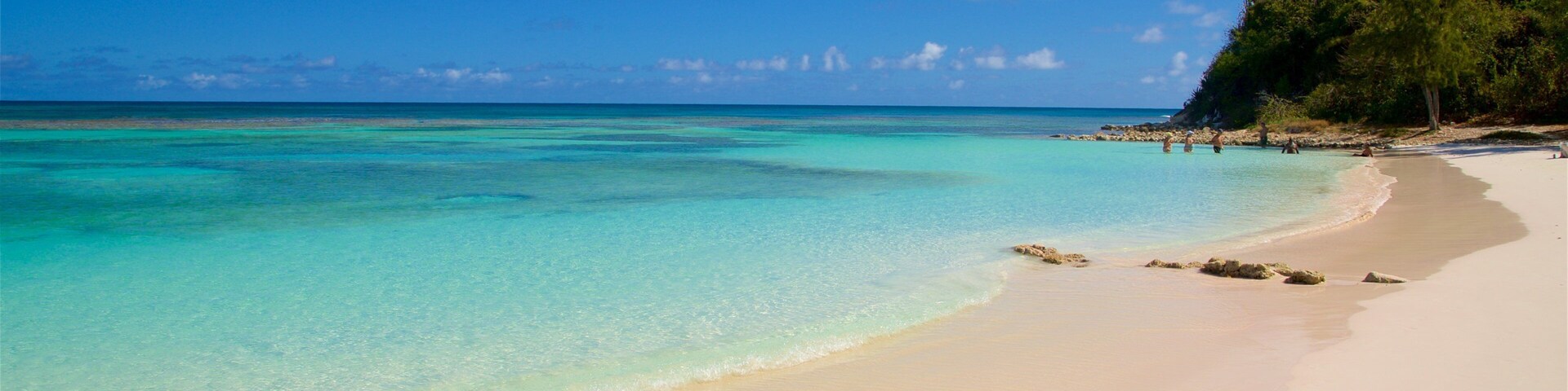 Una playa con aguas turquesas cristalinas, una orilla arenosa y una colina cubierta de vegetación al fondo.