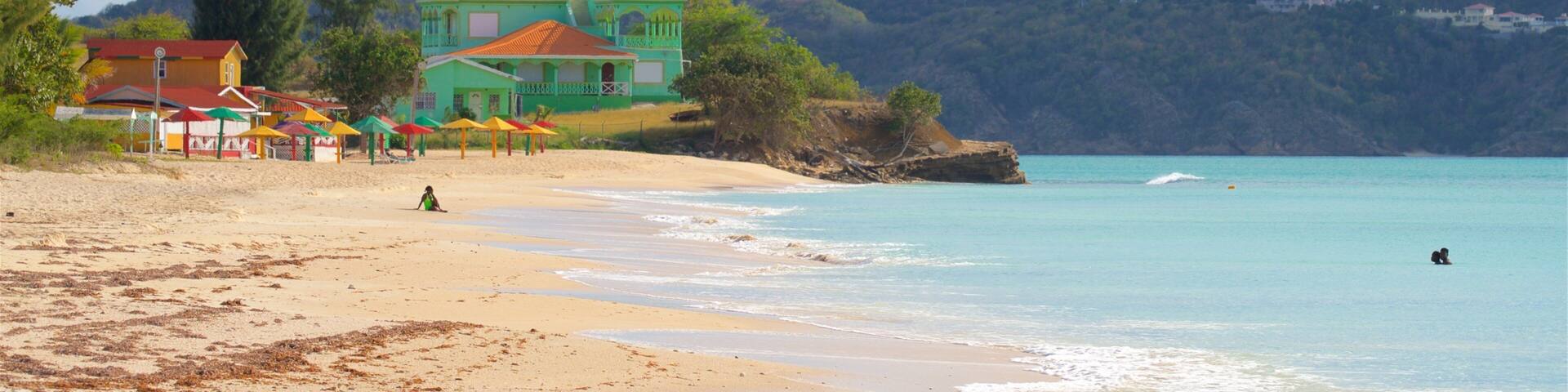A beach with clear turquoise waters, a sandy shore, and a green building with colorful umbrellas.