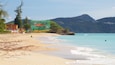 A beach with clear turquoise waters, a sandy shore, and a green building with colorful umbrellas.