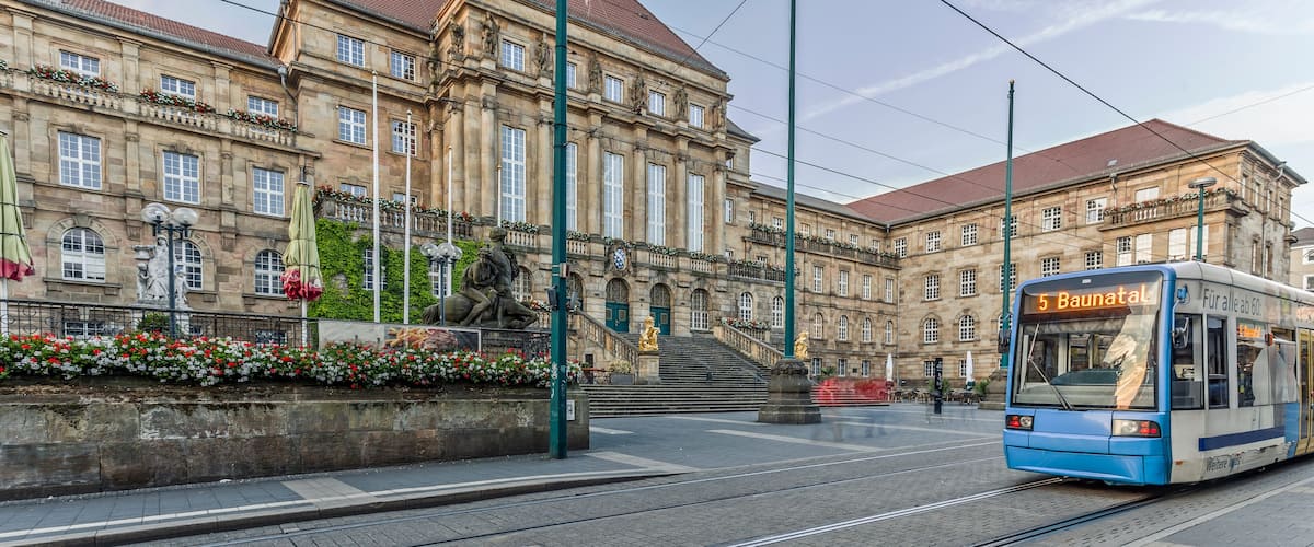 A tram with the number 5 Baunatal approaching a historic building with statues and flower boxes.
