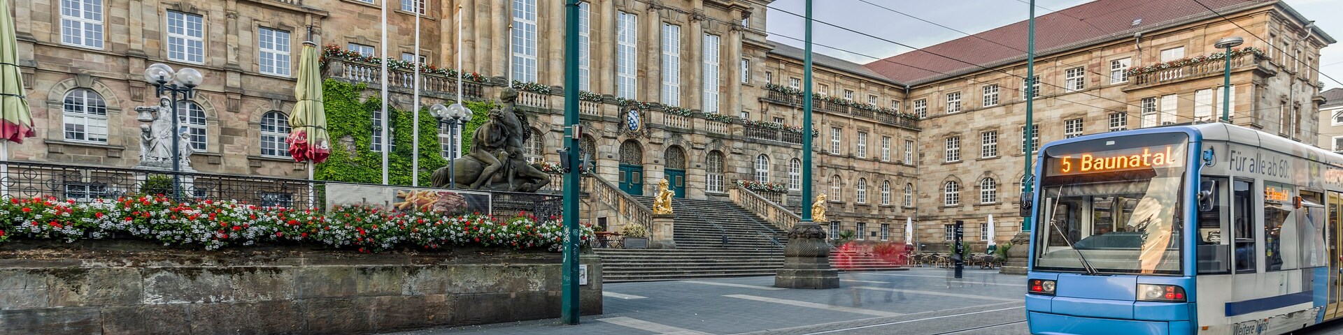 A tram with the number 5 Baunatal approaching a historic building with statues and flower boxes.