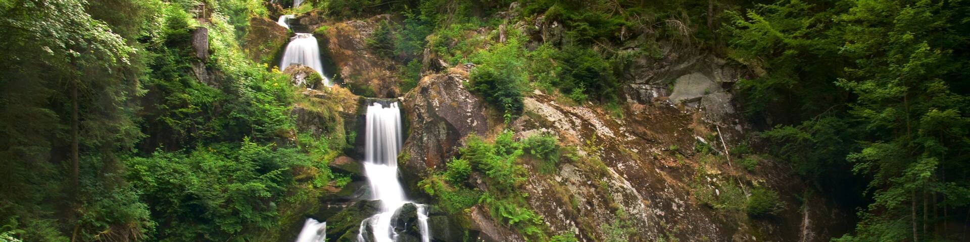 A multi-tiered waterfall surrounded by lush greenery and a viewing platform with people.
