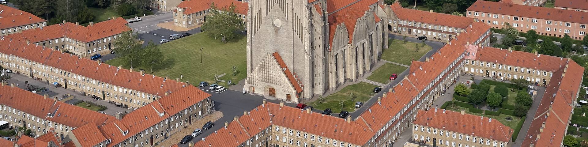 A cathedral with a tall spire, surrounded by residential buildings with red roofs.