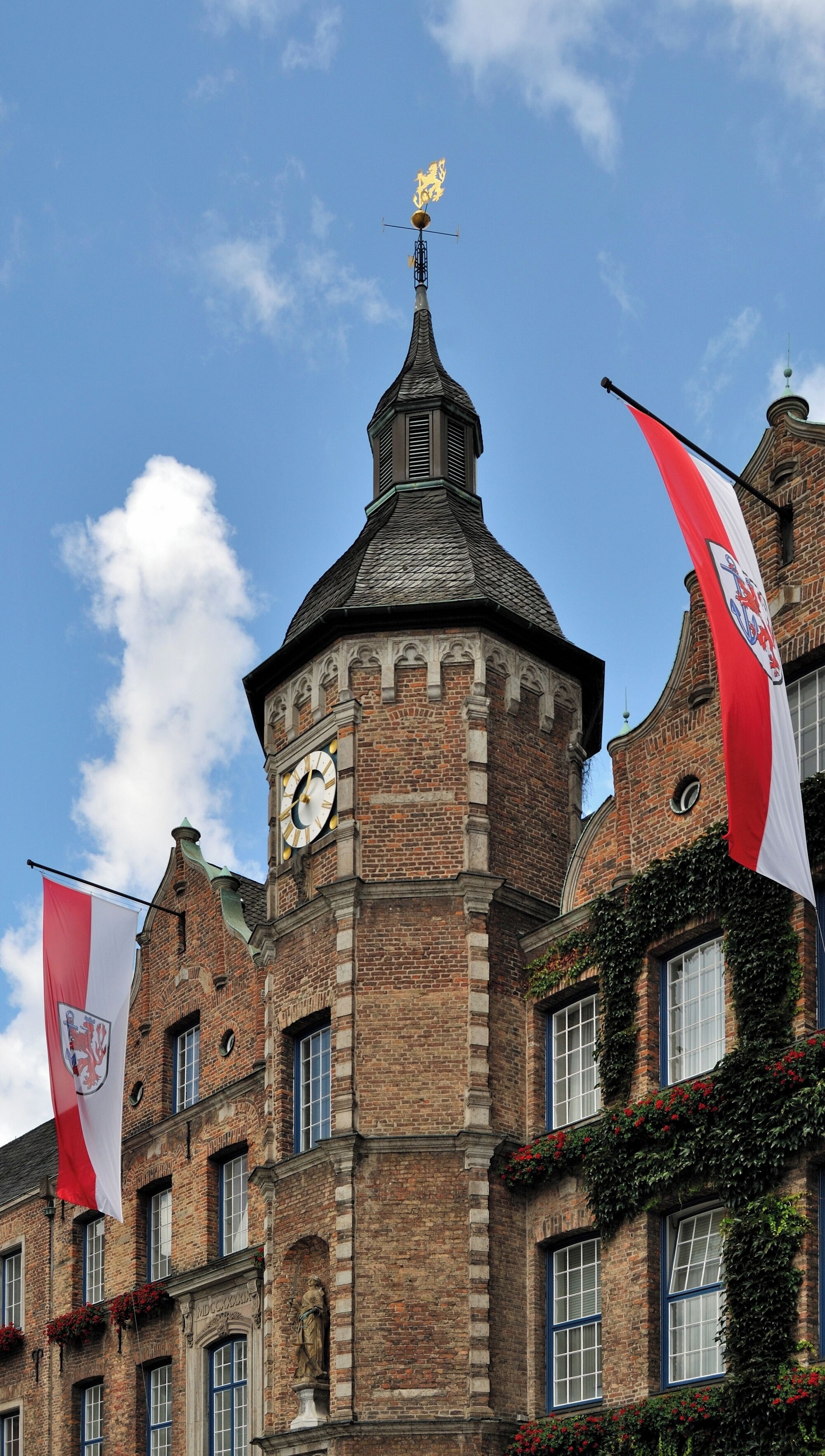Een historisch gebouw met een klokkentoren, rode en witte vlaggen en een windvaan.
