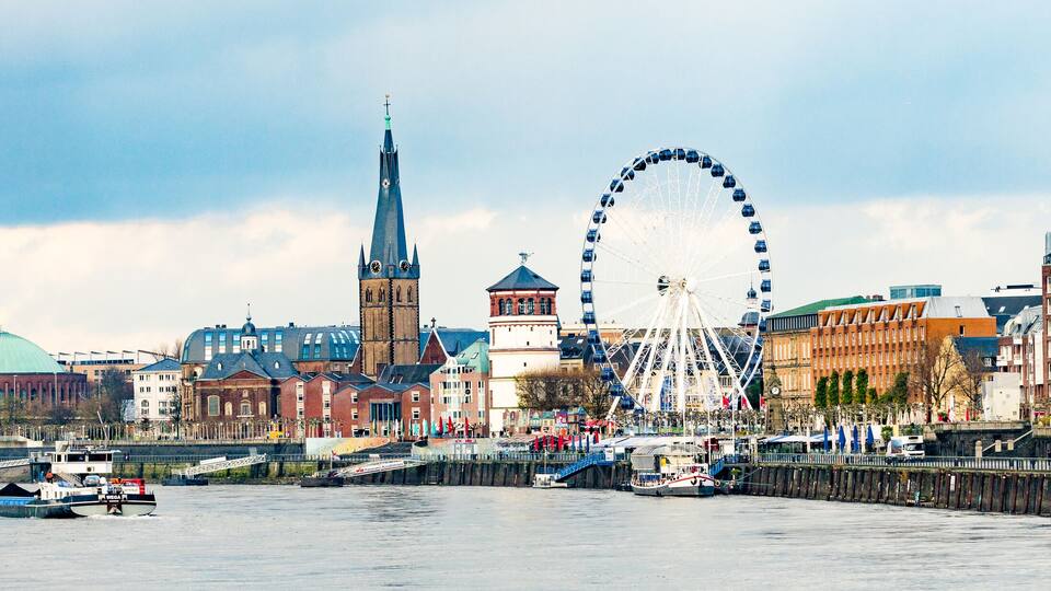 Une vue sur les toits d’une ville, avec un gratte-ciel moderne, le clocher d’une église et une grande roue.