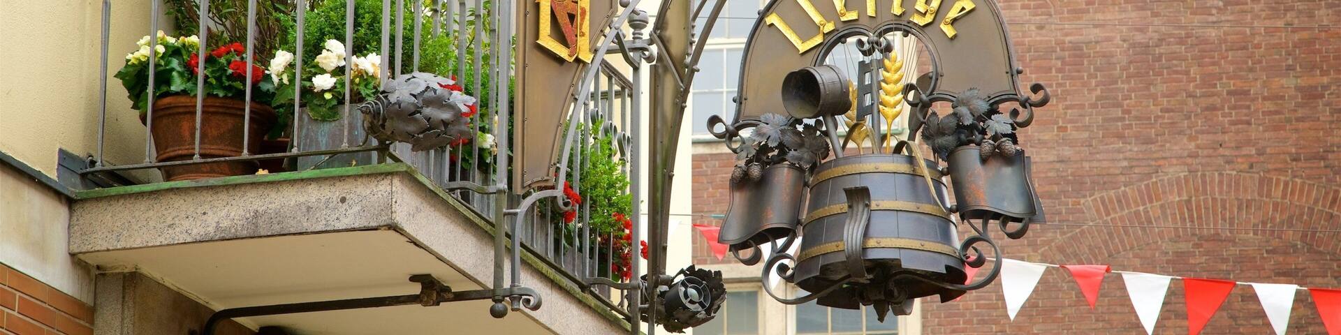 A metal sign with 'Lichtburg' on it, attached to a balcony with potted plants and a metal railing.