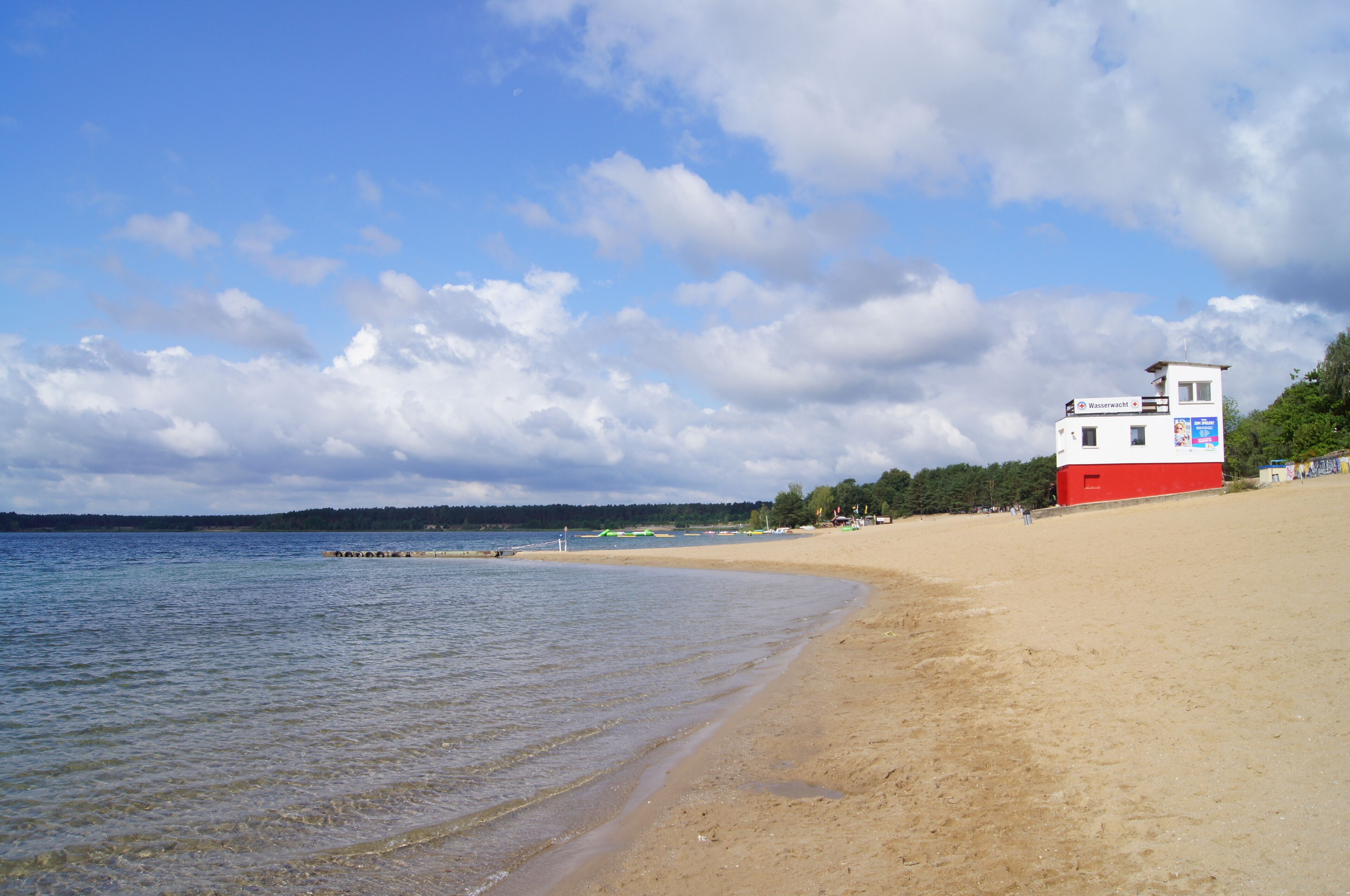 A beach with a red and white building, clear water, and a cloudy sky.