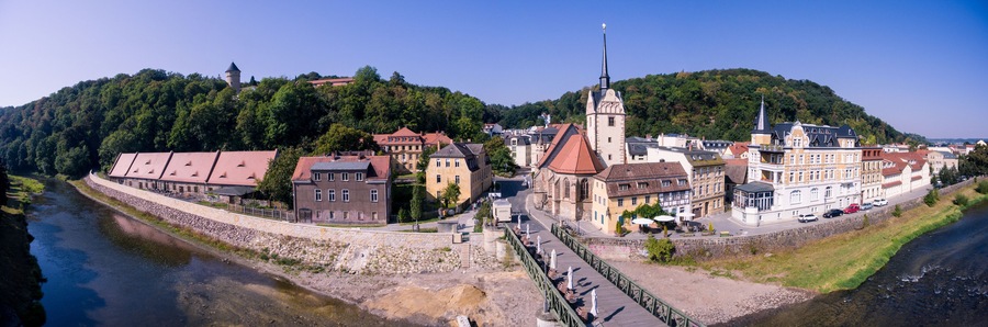 Eine Flussstadt mit historischen Gebäuden, einer markanten Kirche und einer Brücke.