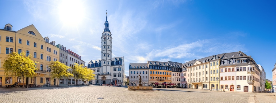 Ein Kopfsteinpflasterplatz mit historischen Gebäuden, einem markanten Glockenturm und einer Statue in der Mitte.