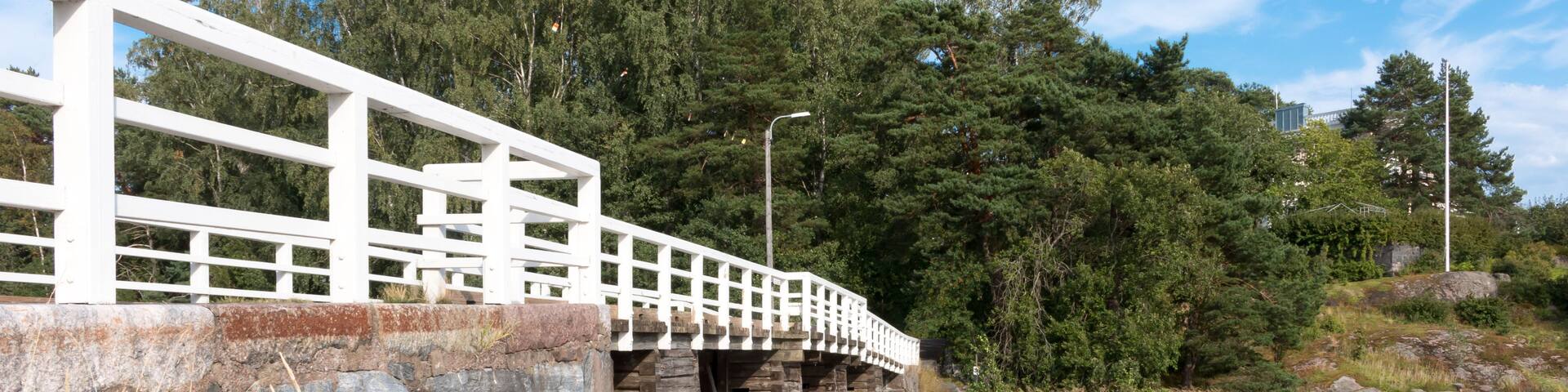 A white bridge over a river with stone walls and trees in the background.