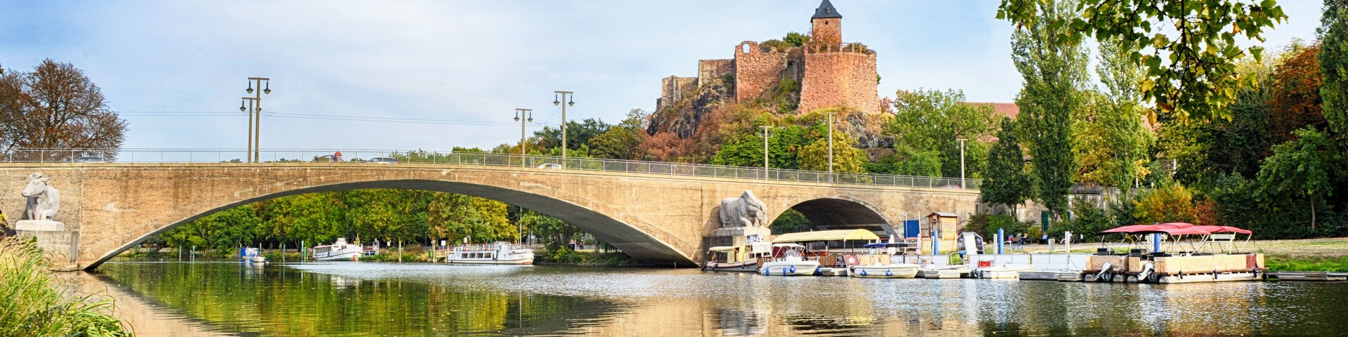 Um rio com uma ponte, um castelo numa colina e barcos.