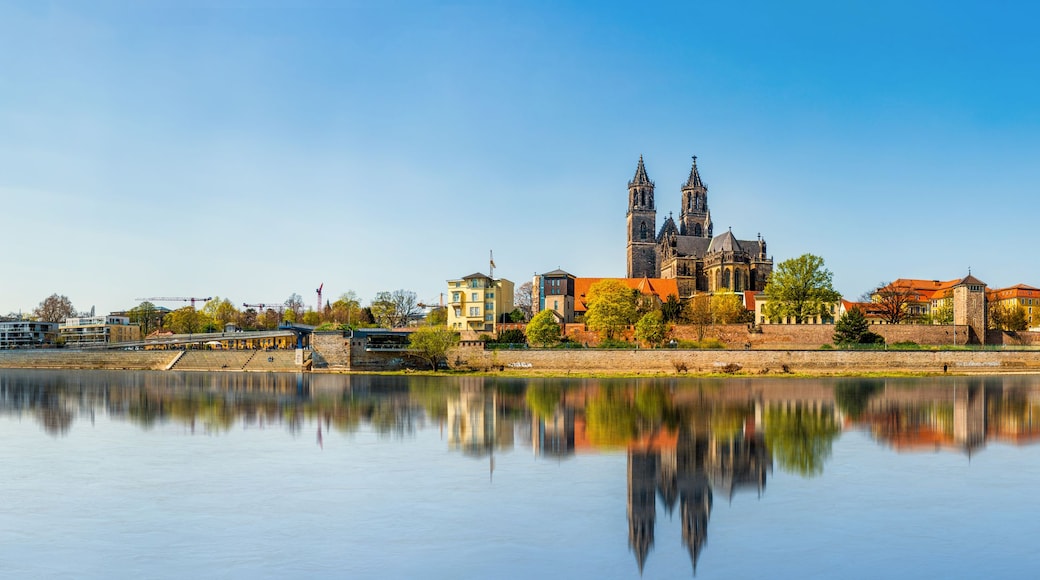 Eine historische Kathedrale mit zwei Türmen, ein ruhiger Fluss im Vordergrund und eine Mischung aus modernen und traditionellen Gebäuden entlang des Ufers.