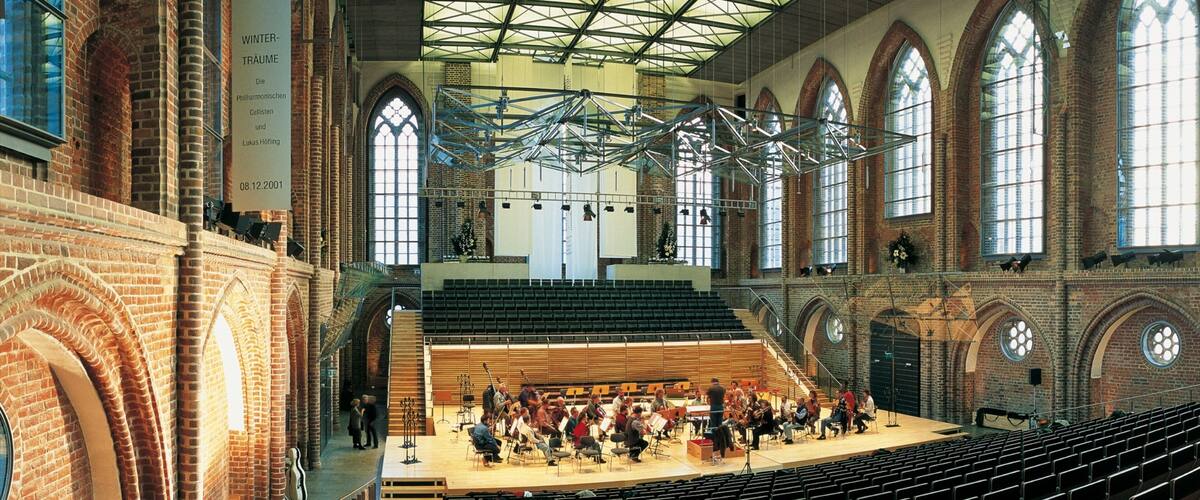 Eine Indoor-Konzerthalle mit einer hohen Gewölbedecke, Backsteinwänden und großen Fenstern.