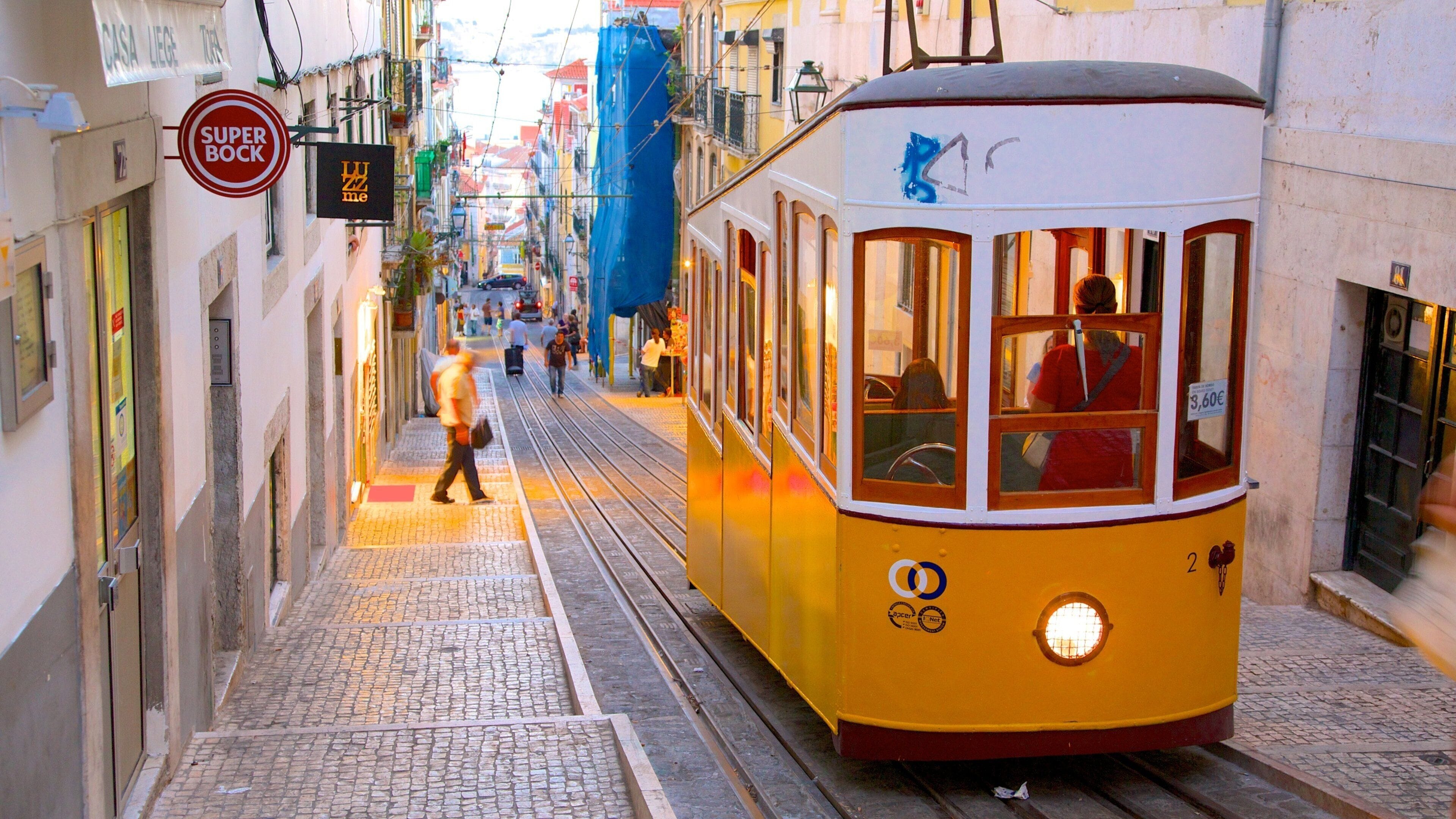 Een gele tram rijdt over een smalle straat met voetgangers en gebouwen.