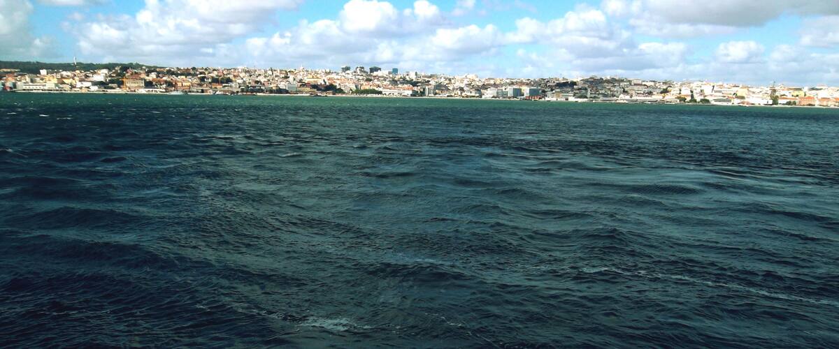 A view of a large body of water with waves, a distant cityscape, and a partly cloudy sky.