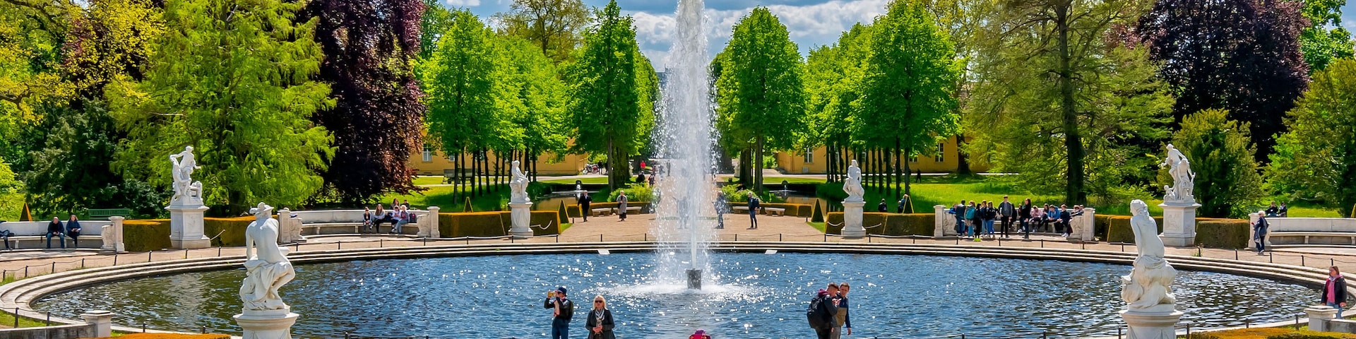 A park with a central fountain, surrounded by manicured lawns and trees.