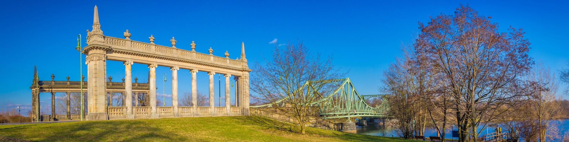 Un edificio clásico con columnas, un puente verde y un parque con árboles.