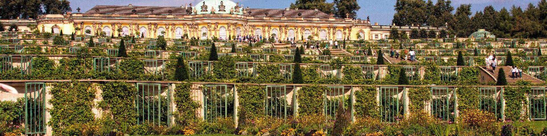 A large, ornate building with a dome, surrounded by manicured gardens and a variety of flowers.