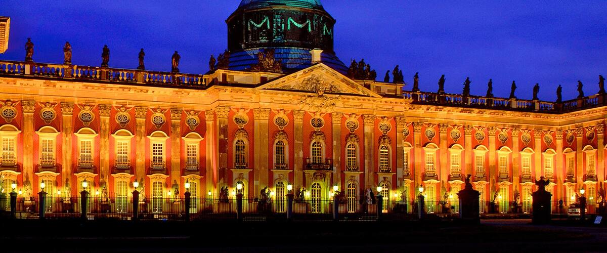 A grand building with a large dome and statues on the roof at dusk.