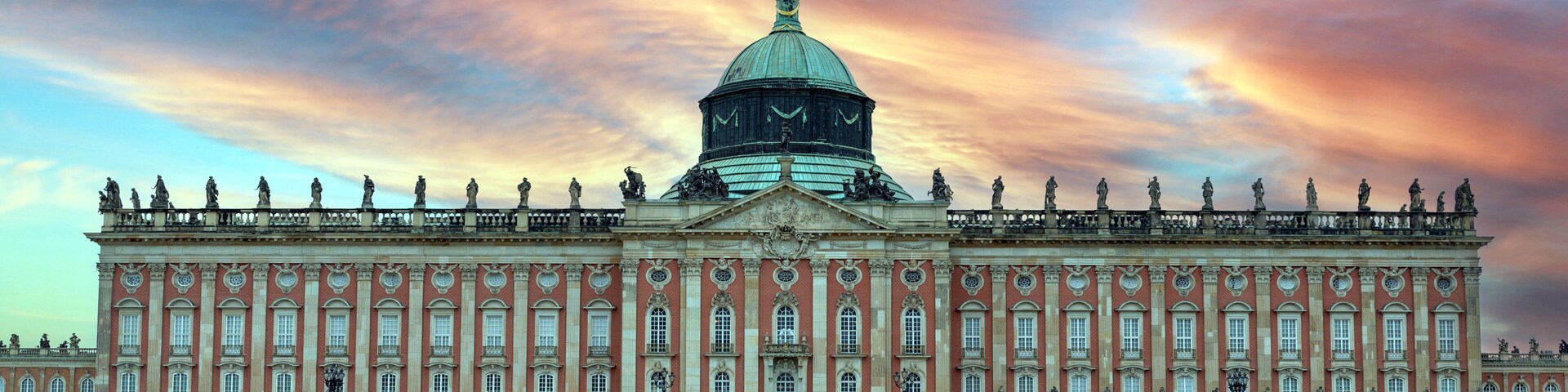 Un edificio grande y histórico con una cúpula destacada y estatuas a lo largo de la fachada.