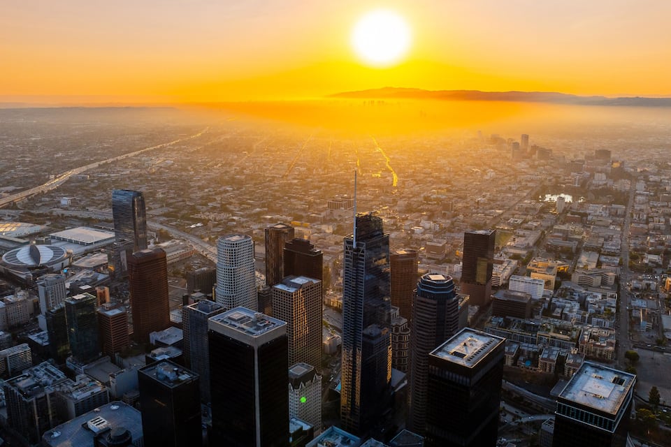 A cityscape with a prominent skyscraper, a large stadium, and a dense urban area during sunset.