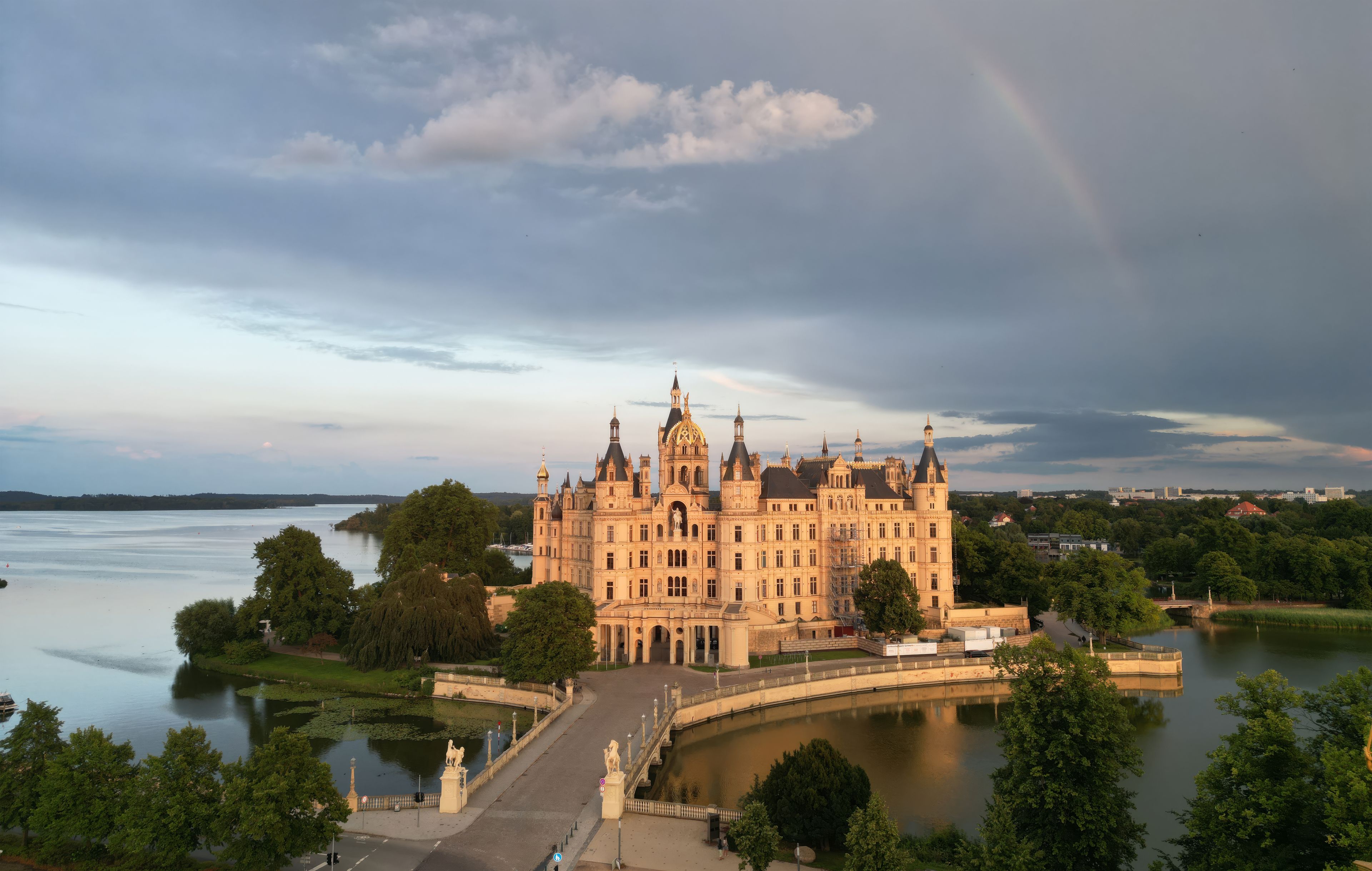 A large, ornate castle by a lake with a rainbow in the sky.