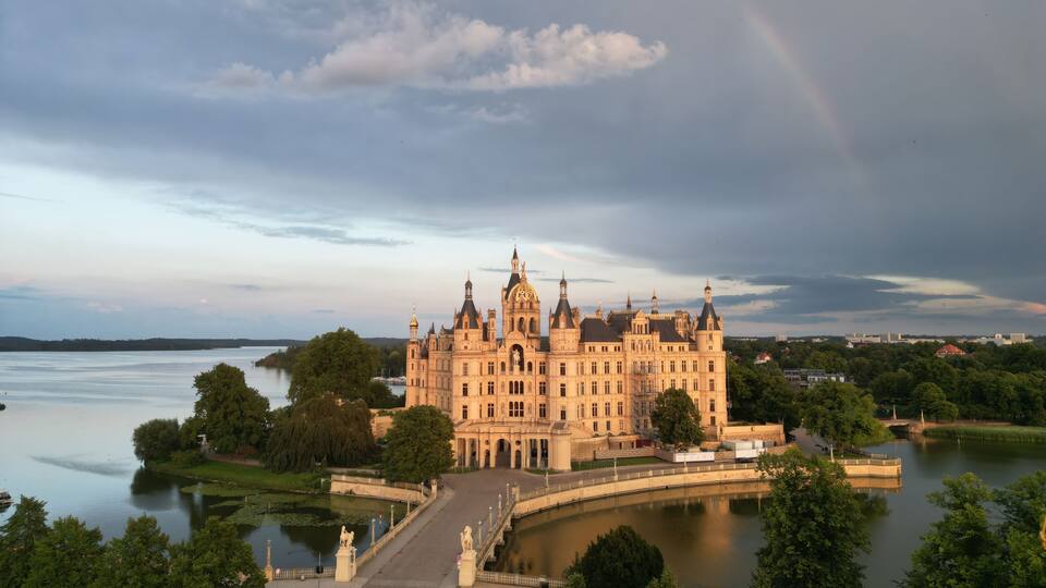 A large, ornate castle by a lake with a rainbow in the sky.