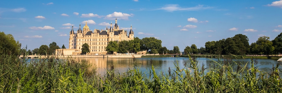 Un castillo imponente junto a un lago tranquilo, rodeado de abundante vegetación.
