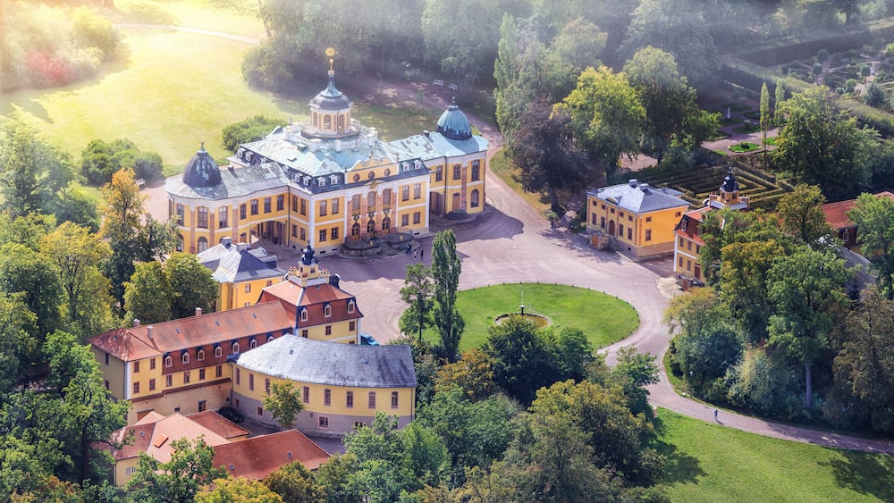 Ein großer, historischer Gebäudekomplex mit mehreren Strukturen, umgeben von üppigem Grün und einem gepflegten Garten.