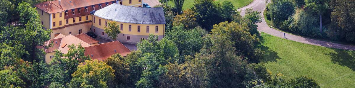 Ein großer, historischer Gebäudekomplex mit mehreren Strukturen, umgeben von üppigem Grün und einem gepflegten Garten.