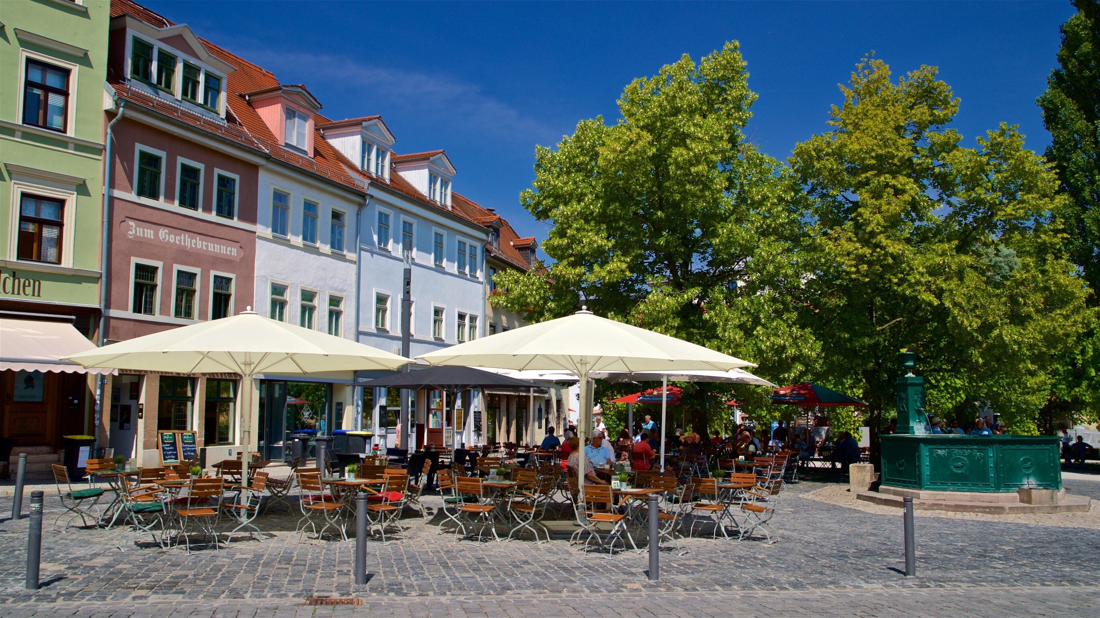 Outdoor cafe seating with umbrellas, cobblestone pavement, and historic buildings in the background.
