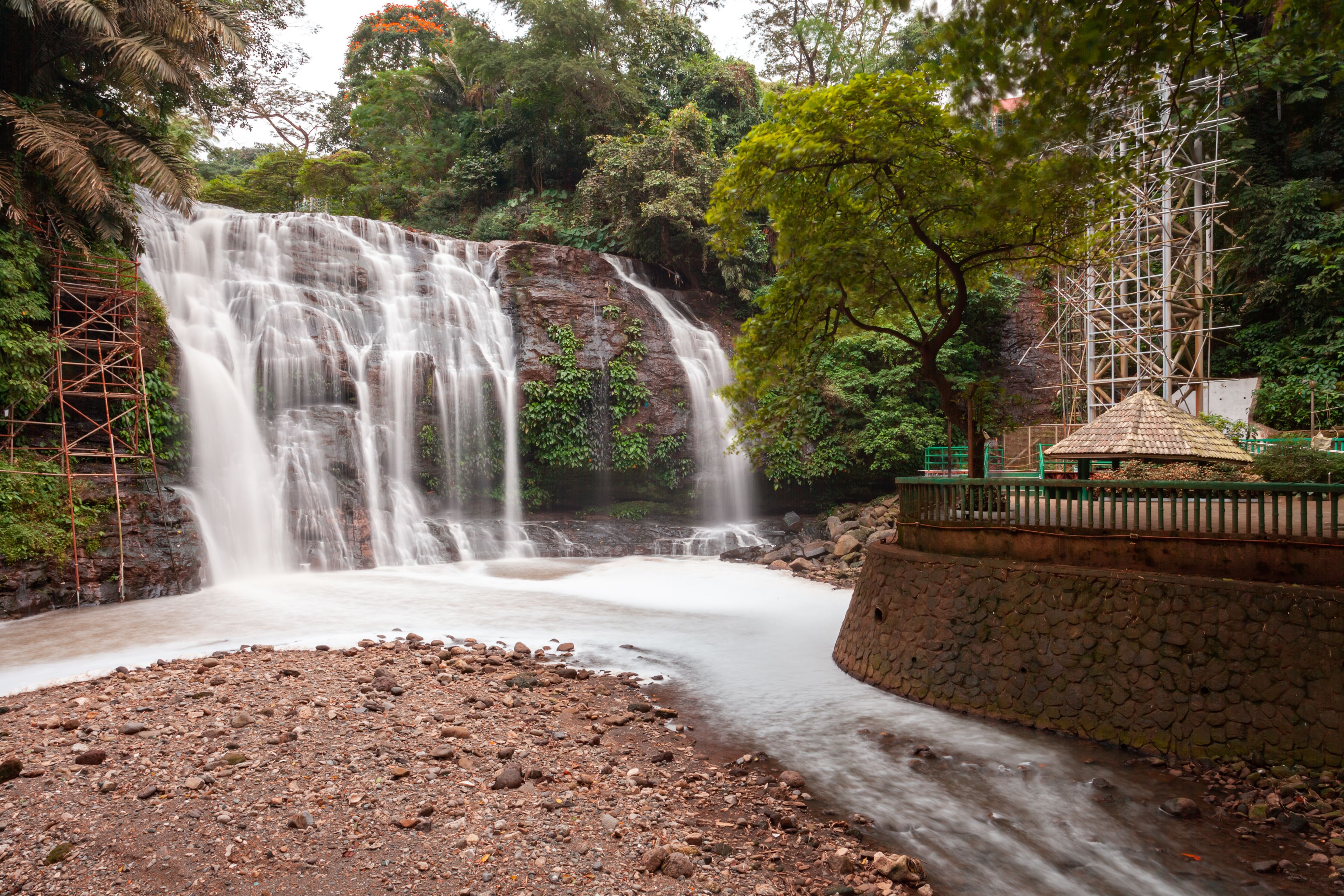 A waterfall cascading over rocks, surrounded by lush greenery and a stone structure.