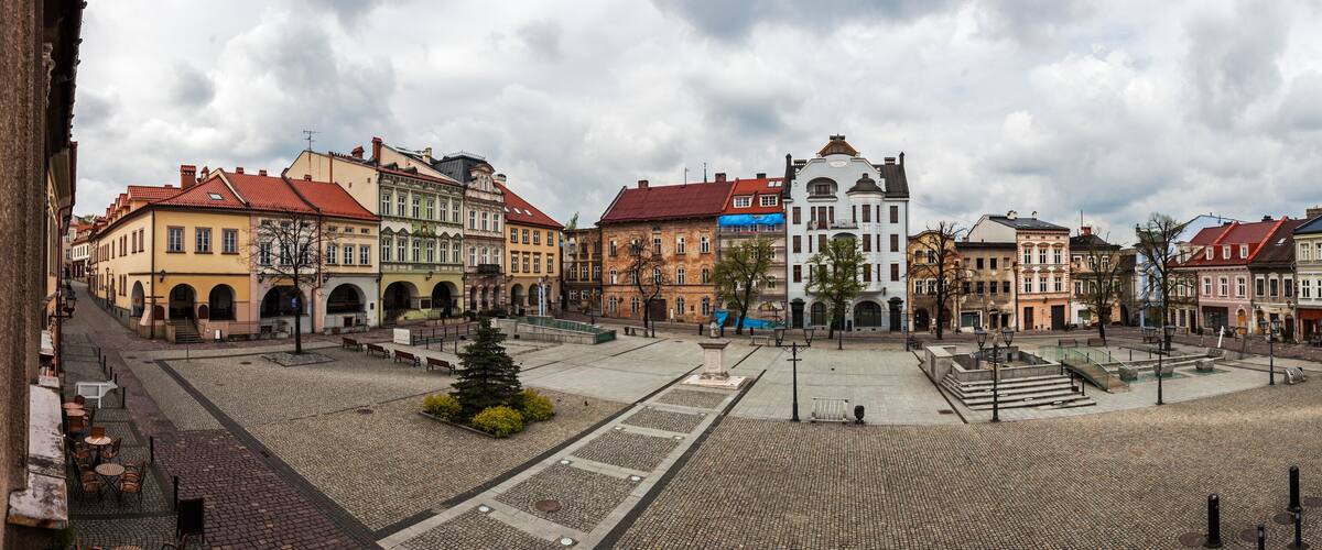 A cobblestone square with historic buildings, a central fountain, and a statue.