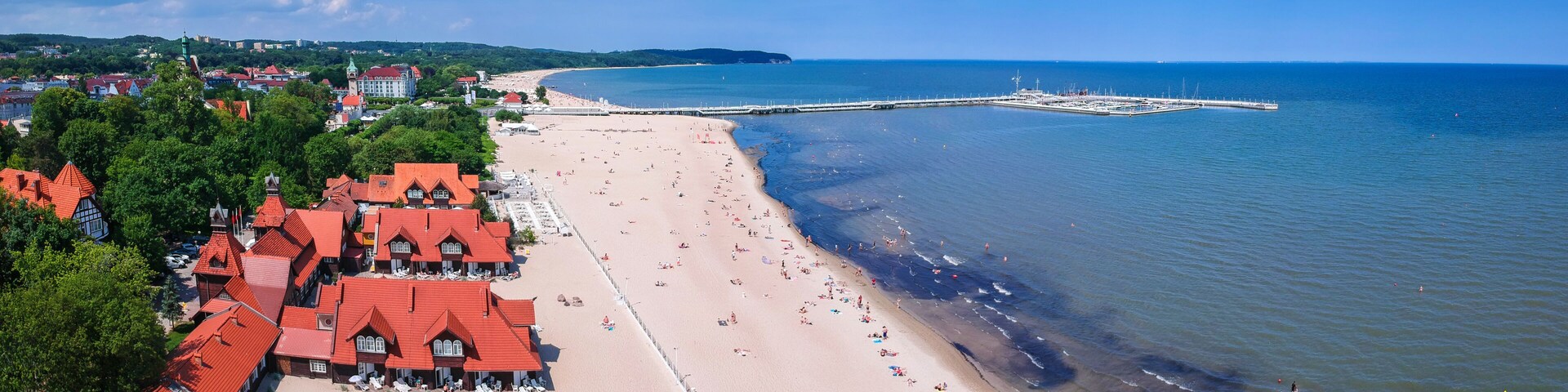 A coastal town with a sandy beach, red-roofed buildings, and a pier extending into the sea.