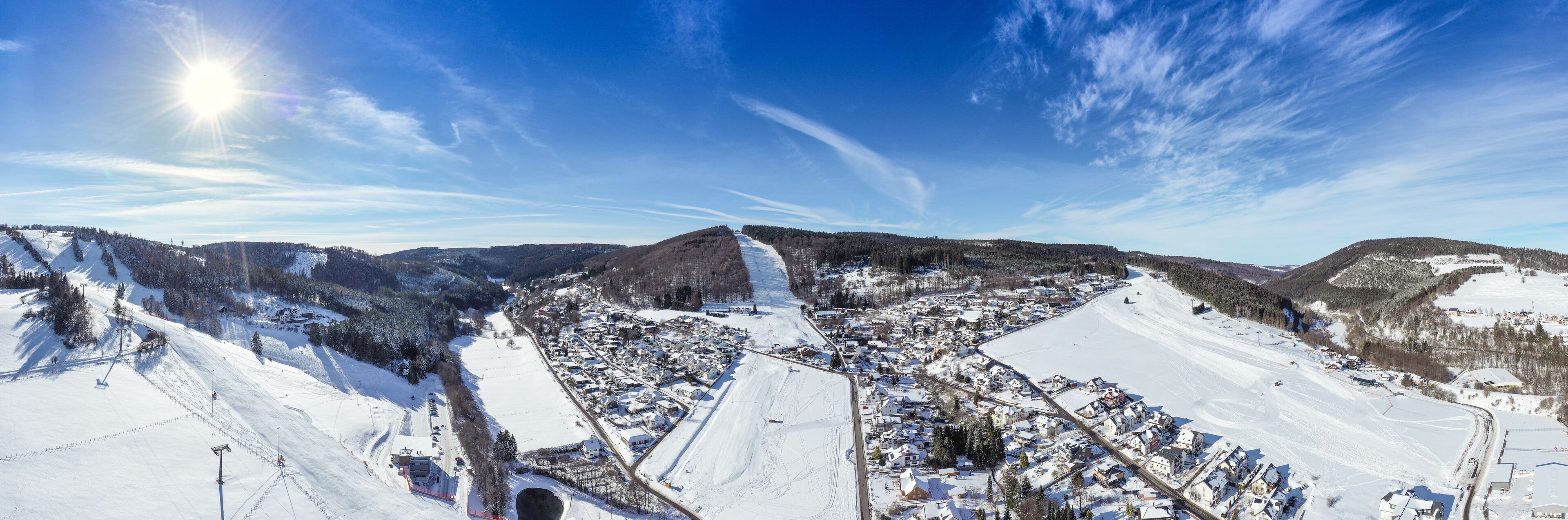 Flight over the vacation resort in Willingen in Hesse. Gastronomy and vacation houses are located next to downhill ski slopes. Wide view.