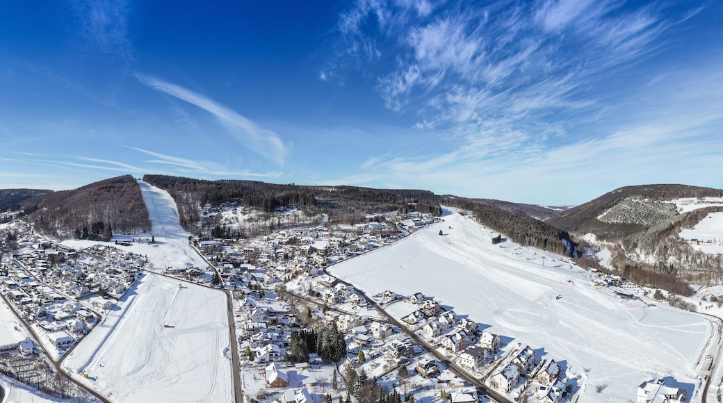 Flight over the vacation resort in Willingen in Hesse. Gastronomy and vacation houses are located next to downhill ski slopes. Wide view.