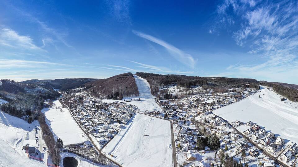 Flight over the vacation resort in Willingen in Hesse. Gastronomy and vacation houses are located next to downhill ski slopes. Wide view.
