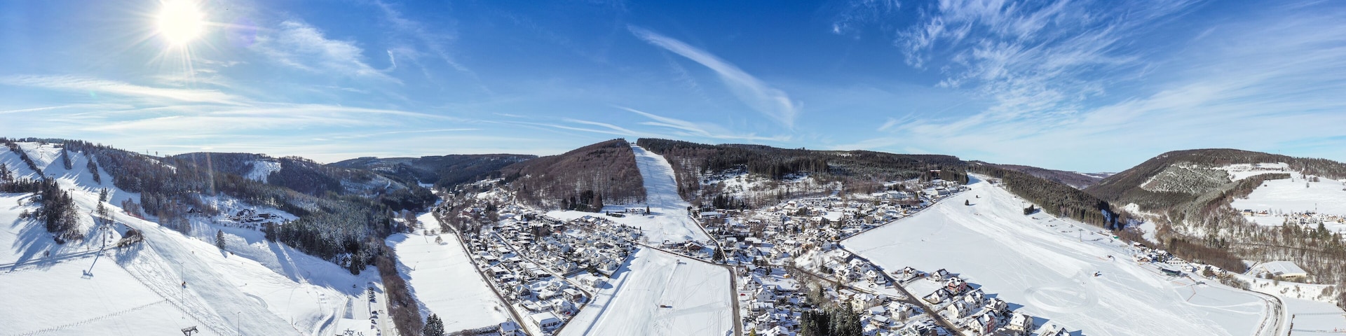 Flight over the vacation resort in Willingen in Hesse. Gastronomy and vacation houses are located next to downhill ski slopes. Wide view.