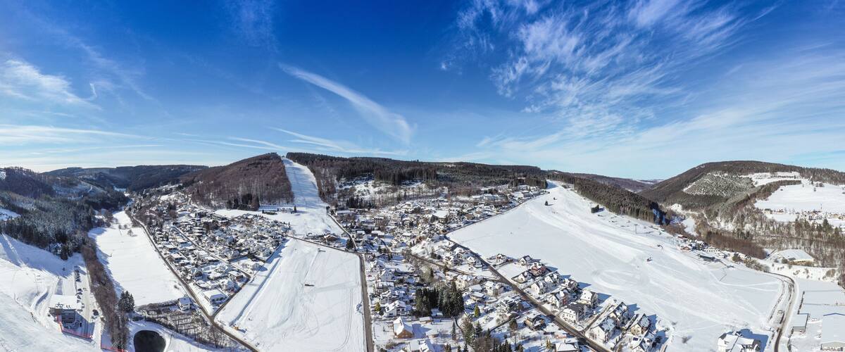 Flight over the vacation resort in Willingen in Hesse. Gastronomy and vacation houses are located next to downhill ski slopes. Wide view.